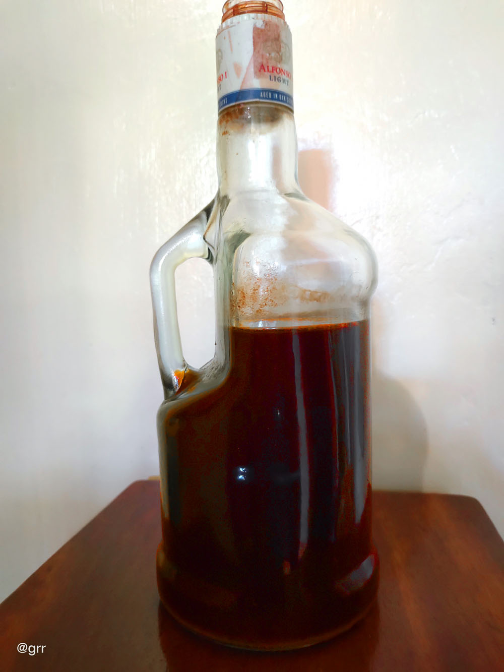 A dark red bahalina placed on a huge Alfonso bottle.