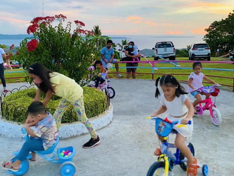 Kids playing with bicycles while adults supervise them nearby.