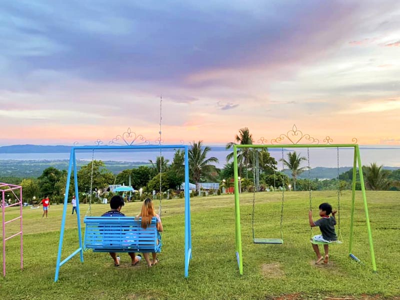 People sitting on the swing with an overlooking view of the sea and islands.
