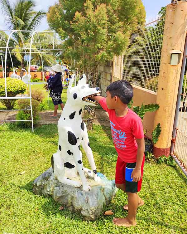 A kid inserting his hand inside the mouth of a dog statue.