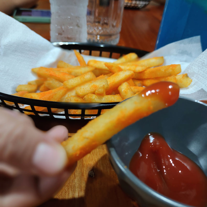 Dipping a French fries on a ketchup sauce.