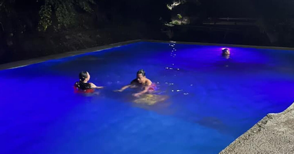Guests enjoying night swimming in the blue-lit swimming pool.