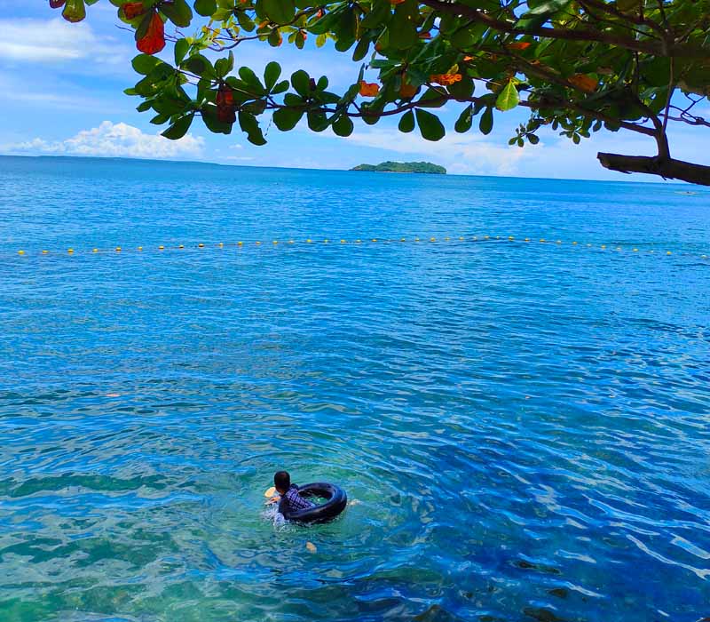 A guest swimming with floaters on the clear blue waters while looking at Dalutan Island